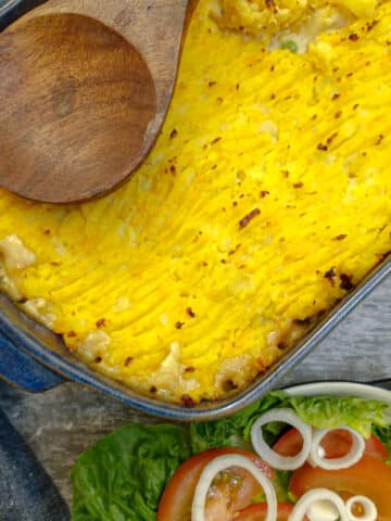 A dish of leftover shepherd's pie topped with potato and sweet potato mash, with a dish of green salad in the foreground.