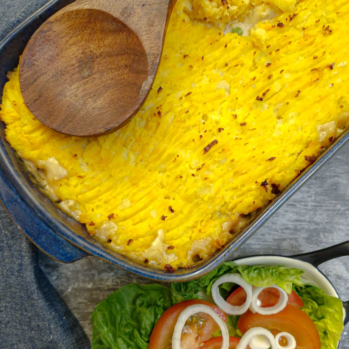A dish of leftover shepherd's pie topped with potato and sweet potato mash, with a dish of green salad in the foreground.