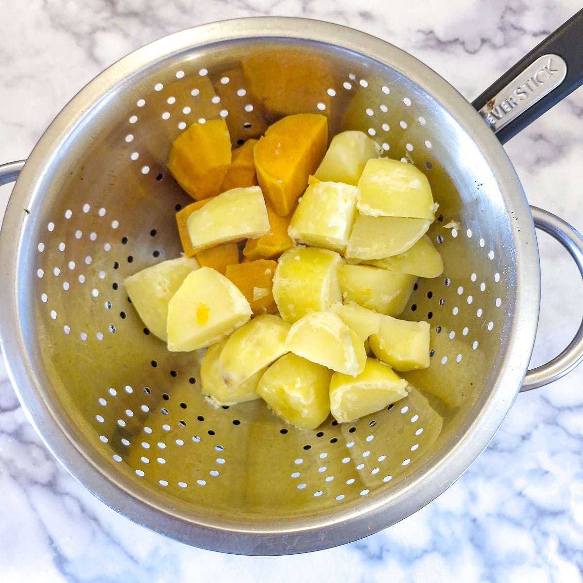 Boiled potatoes and sweet potatoes draining in a colander.