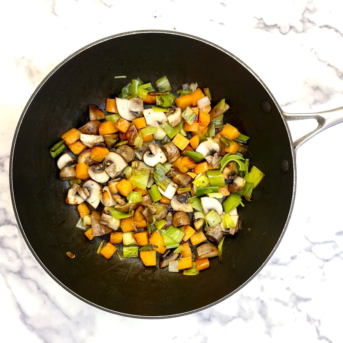Diced leeks, carrots and mushrooms softening in a saute pan.