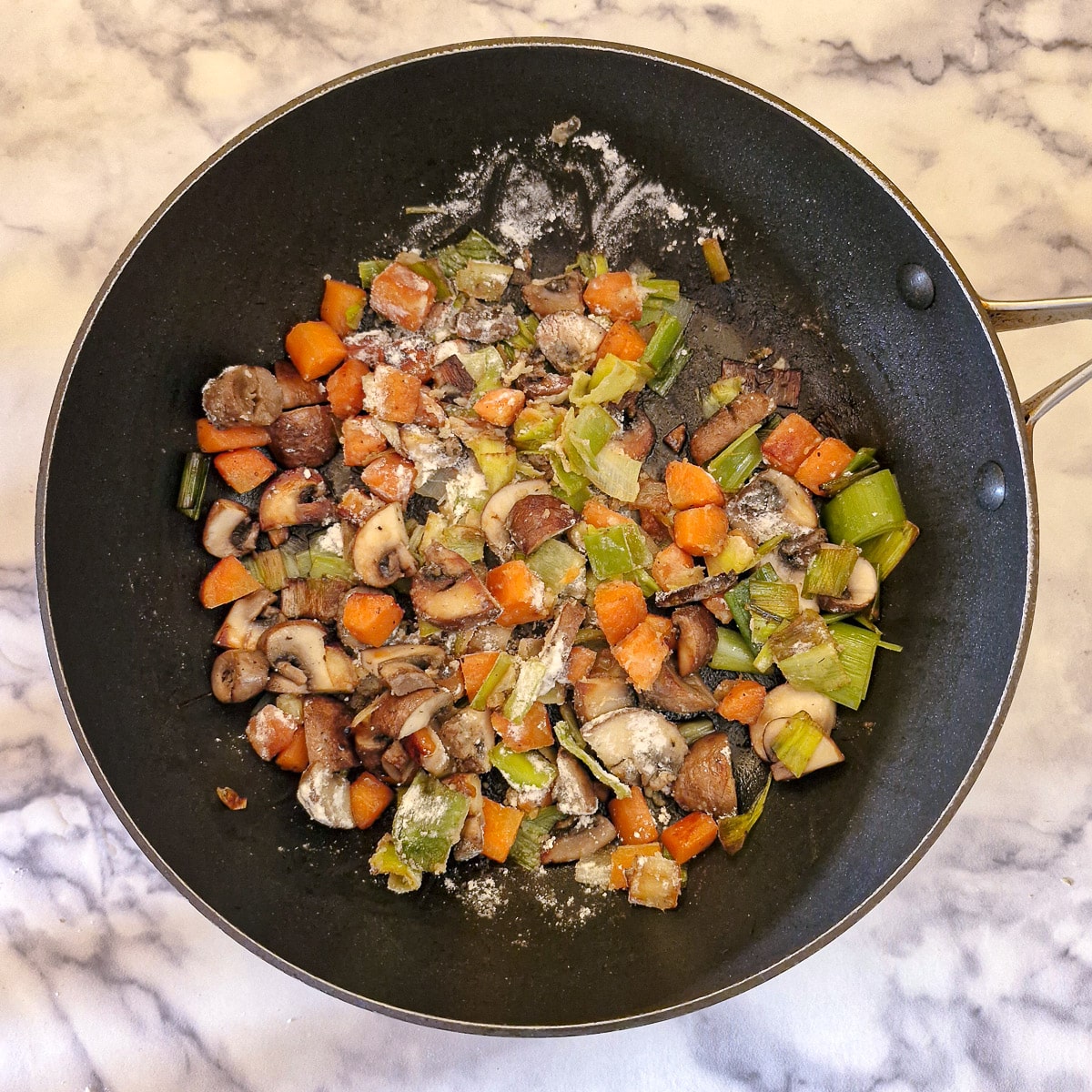 Flour stirred into the vegetables in a saute pan.