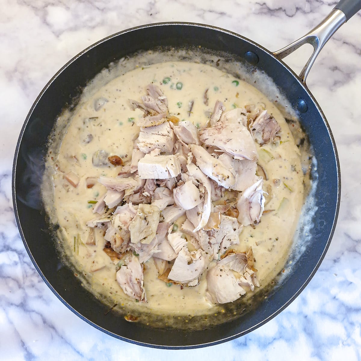 Diced leftover cooked chicken being added to the creamy vegetable sauce.
