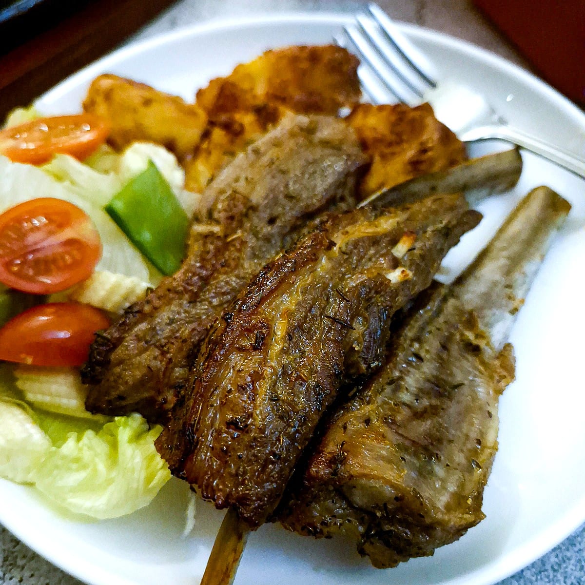 Three lamb ribs on a plate with tomatoes and lettuce.