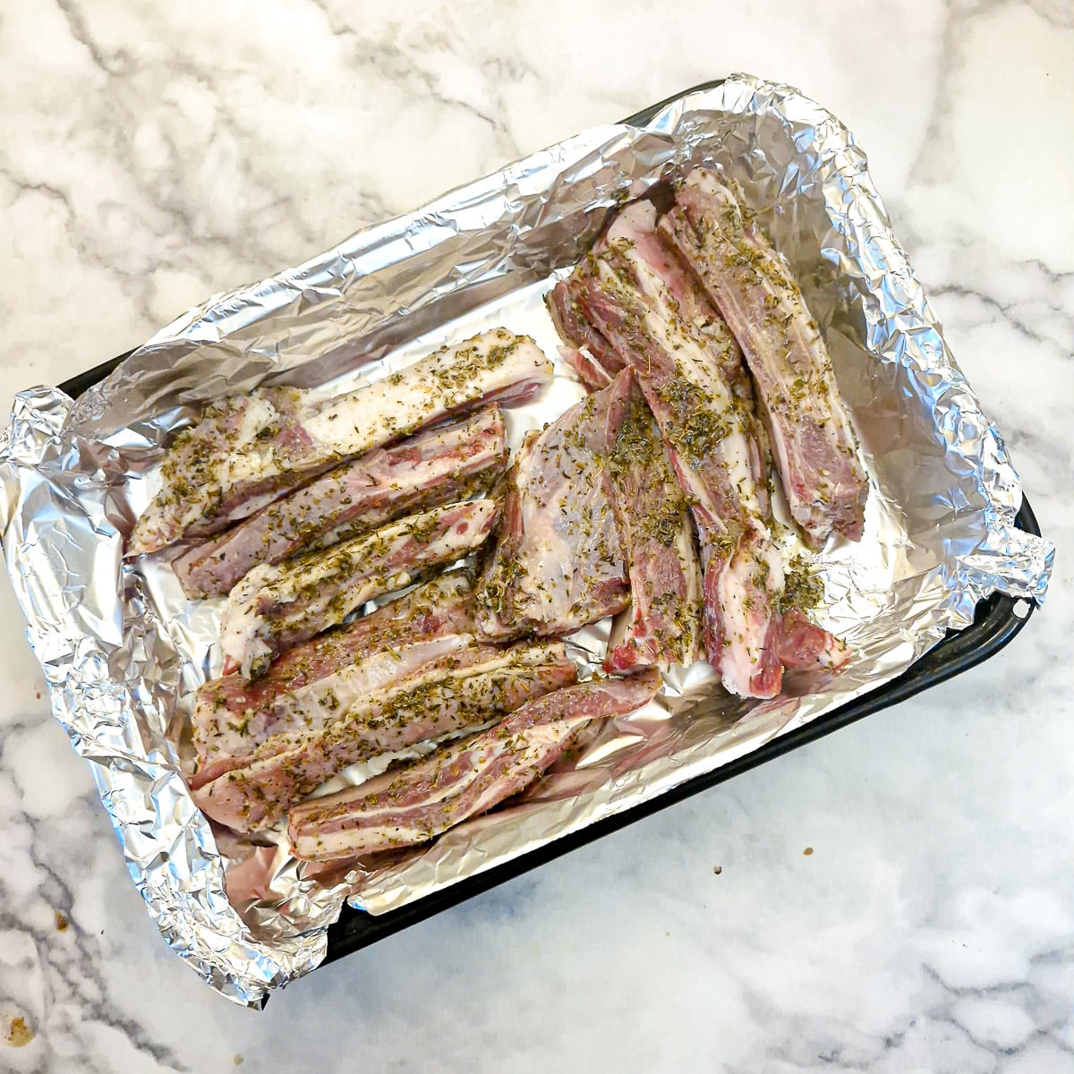 Lamb ribs arranged in a single layer in a foil-lined roasting pan.