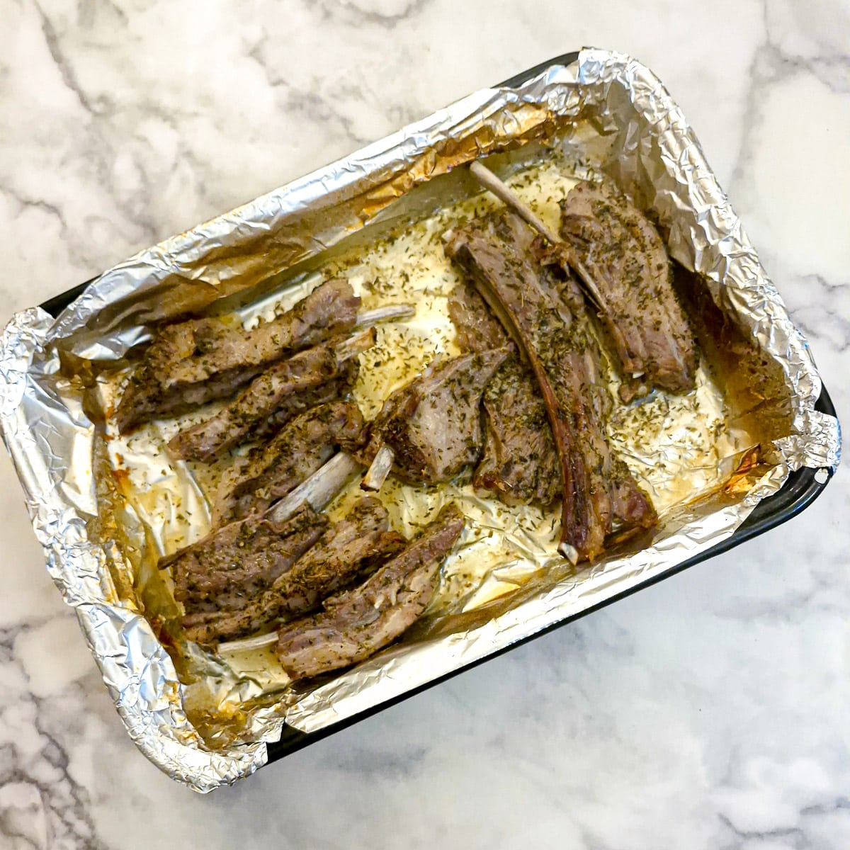 Cooked lamb ribs in a roasting pan before being browned in the oven.