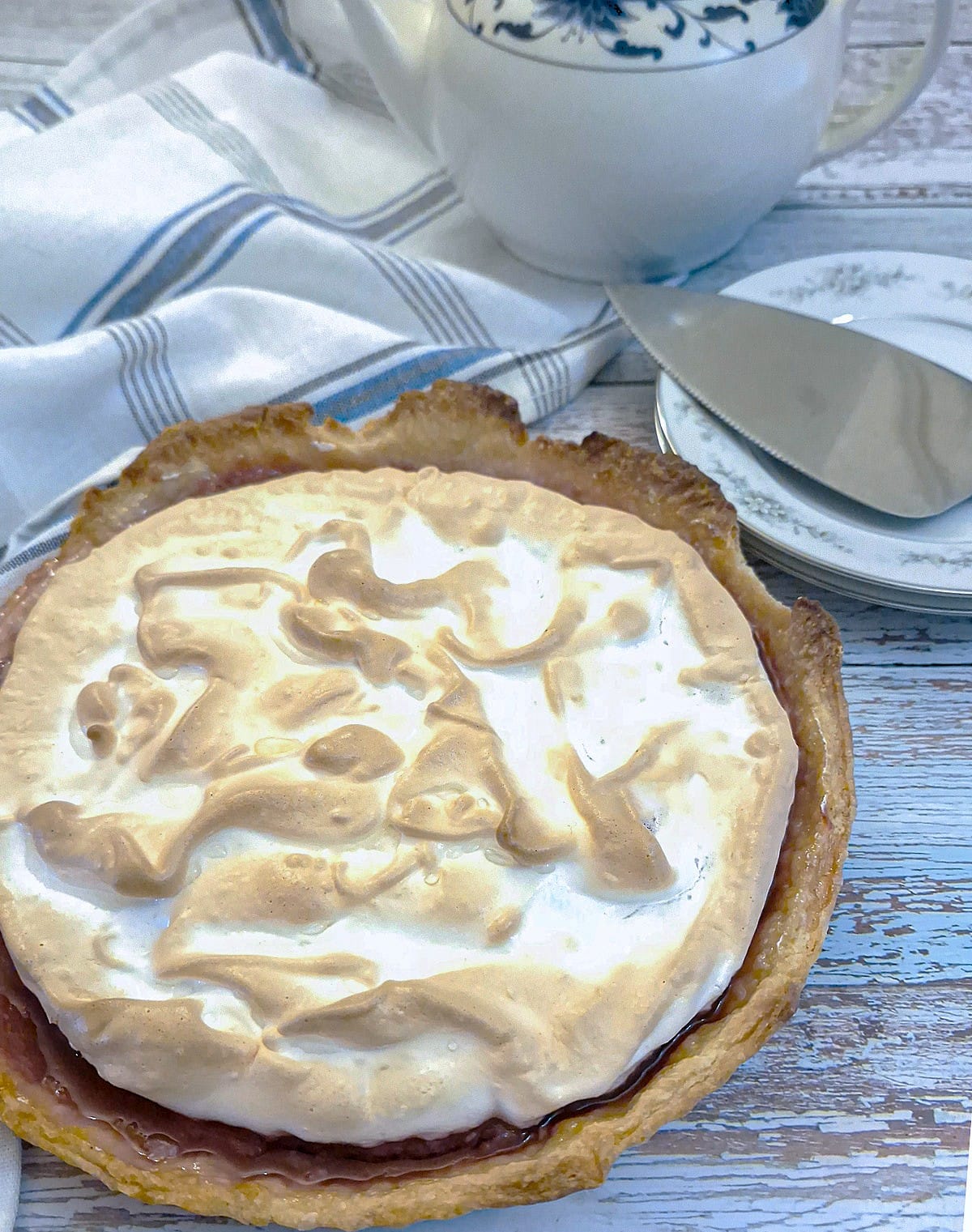 A raspberry meringue pie on a tea table before it has been sliced. The meringue is lightly browned and fluffy.