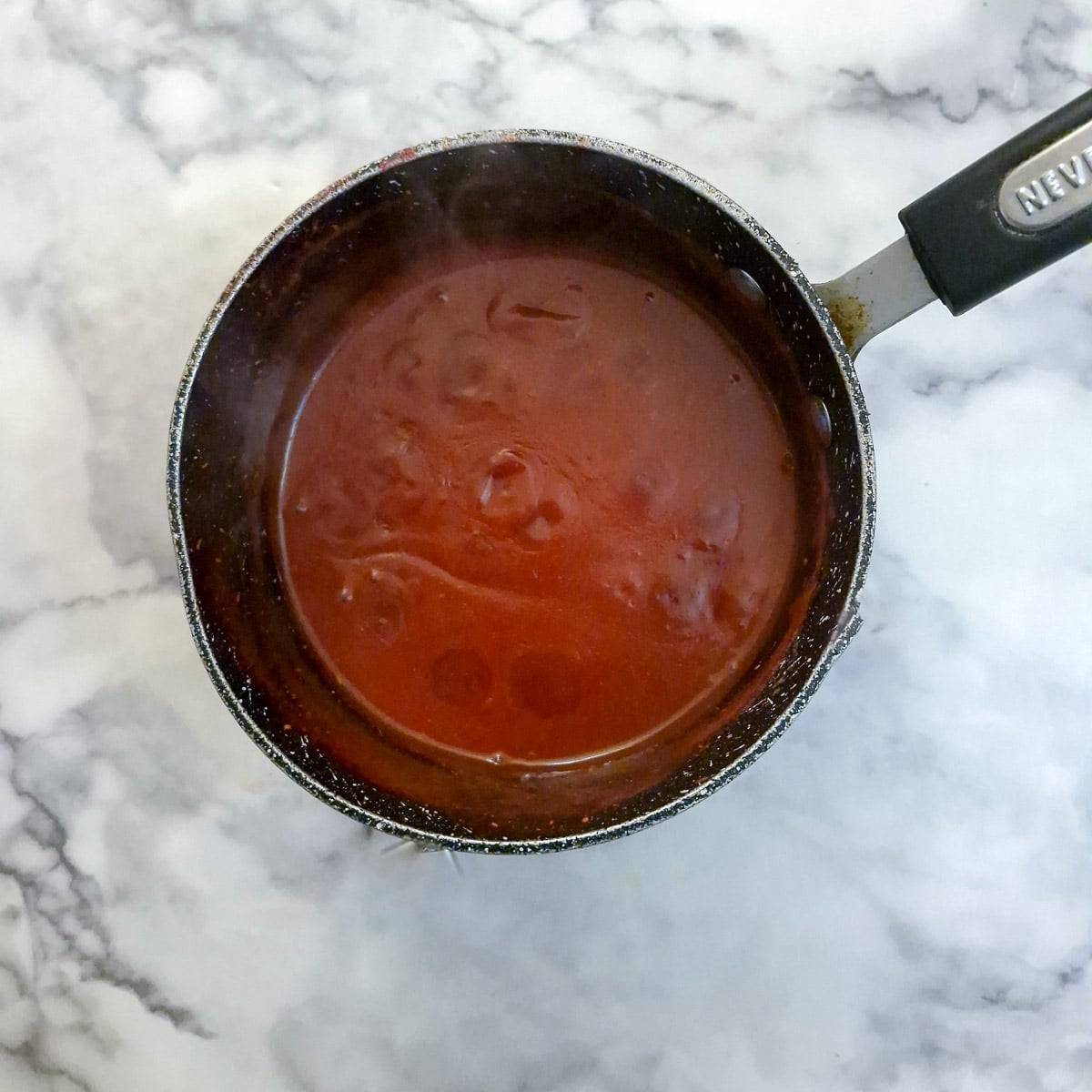 Raspberry curd thickening in a saucepan. There are 'craters' on top of the curd which form once the curd thickens.