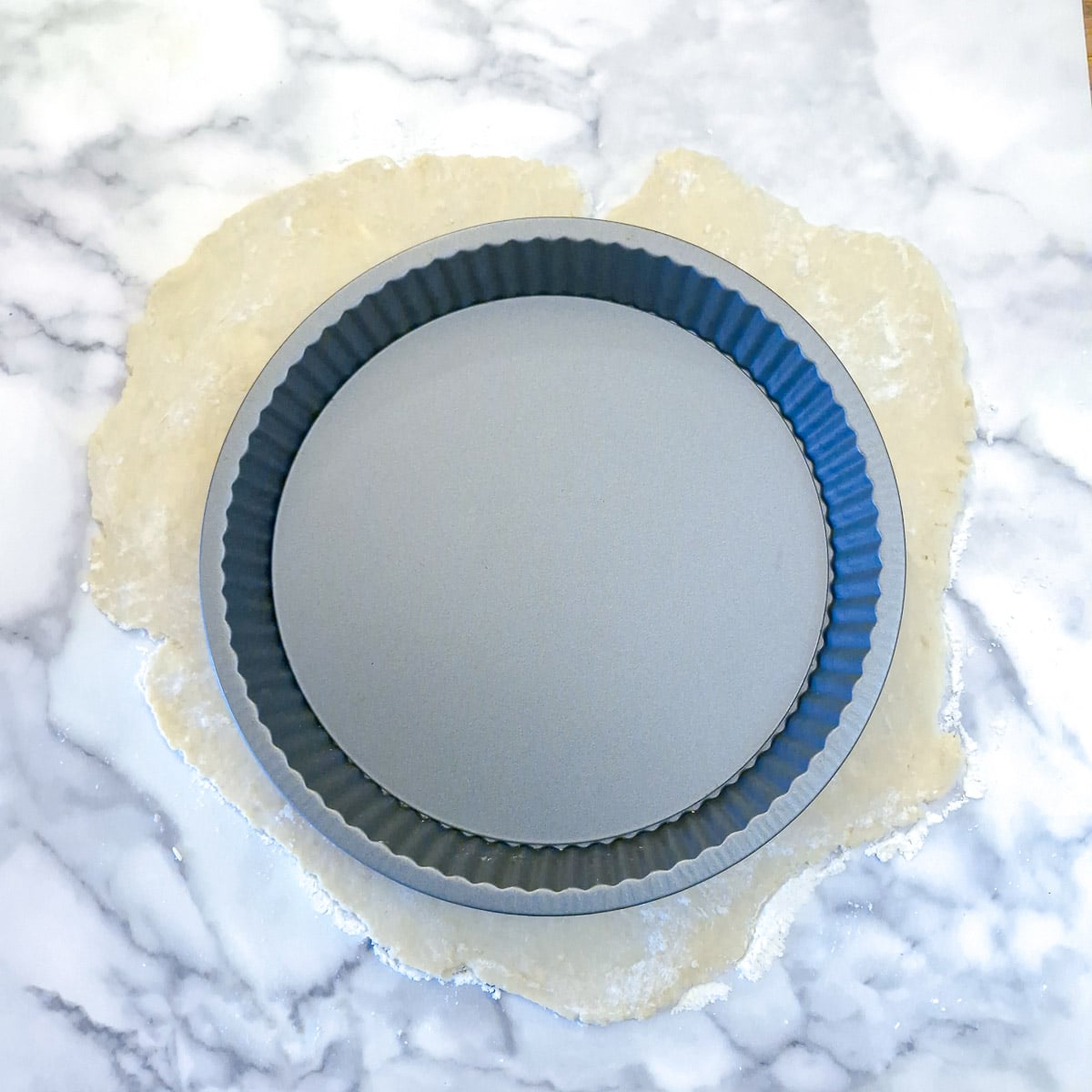 Thinly rolled pastry on a counter top with a baking dish on top to make sure the pastry will fit.