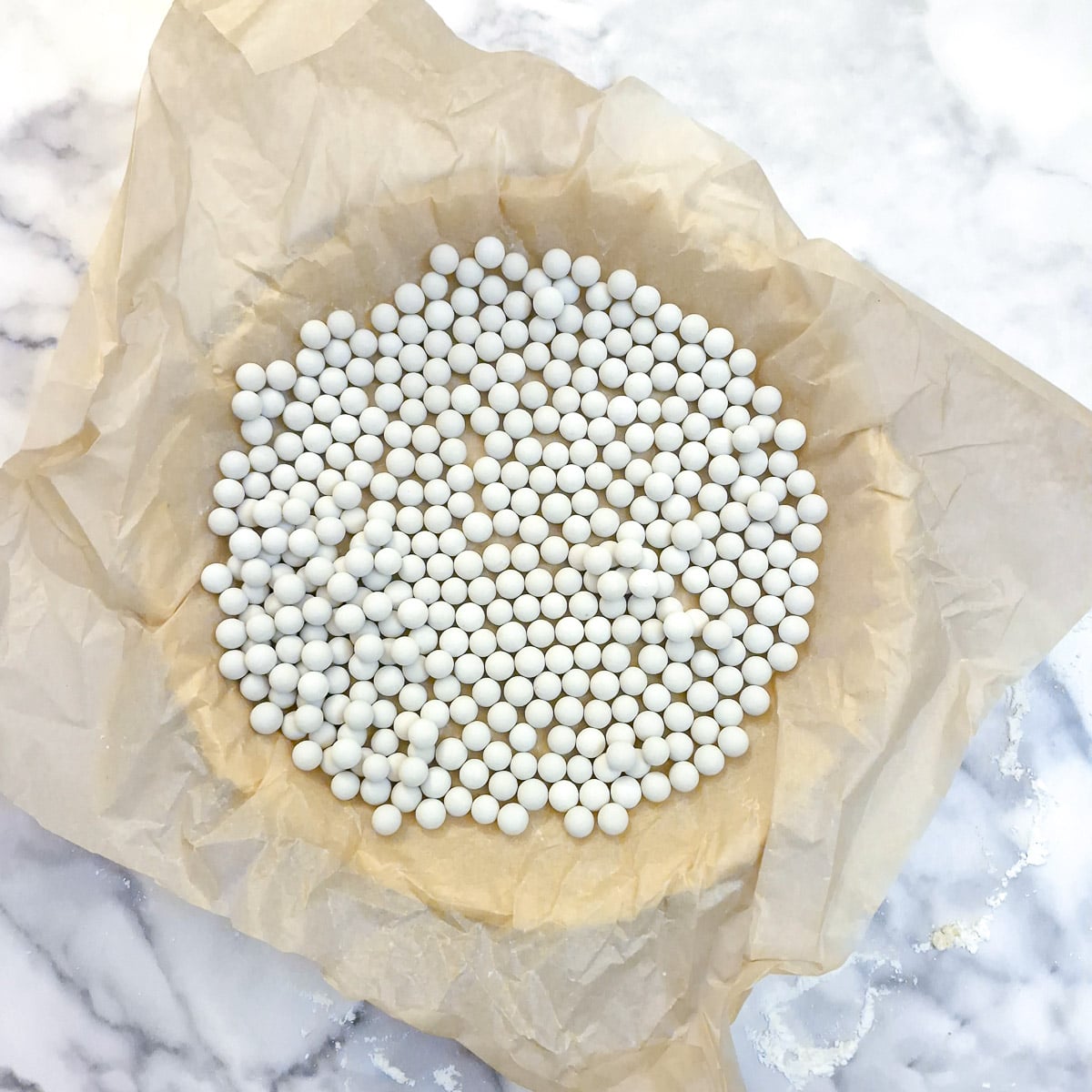 Ceramic baking beads on a layer of baking parchment covering the pastry before baking.