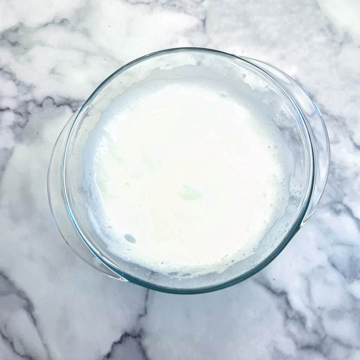 Egg whites mixed to soft peaks in a large glass bowl.