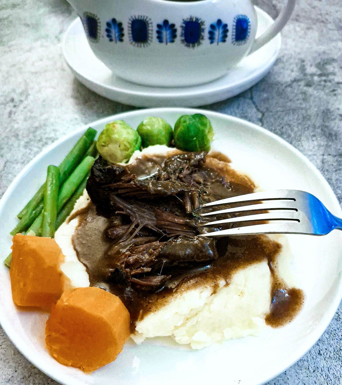Beef cheeks on a pile of mashed potatoes with steamed vegetables amd gravy.