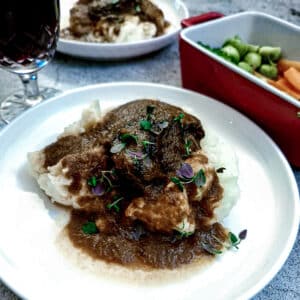 A piece of slow-braised beef cheek on a pile of mashed potatoes, with gravy.