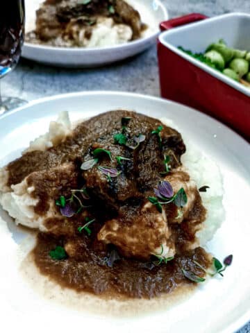 A piece of slow-braised beef cheek on a pile of mashed potatoes, with gravy.