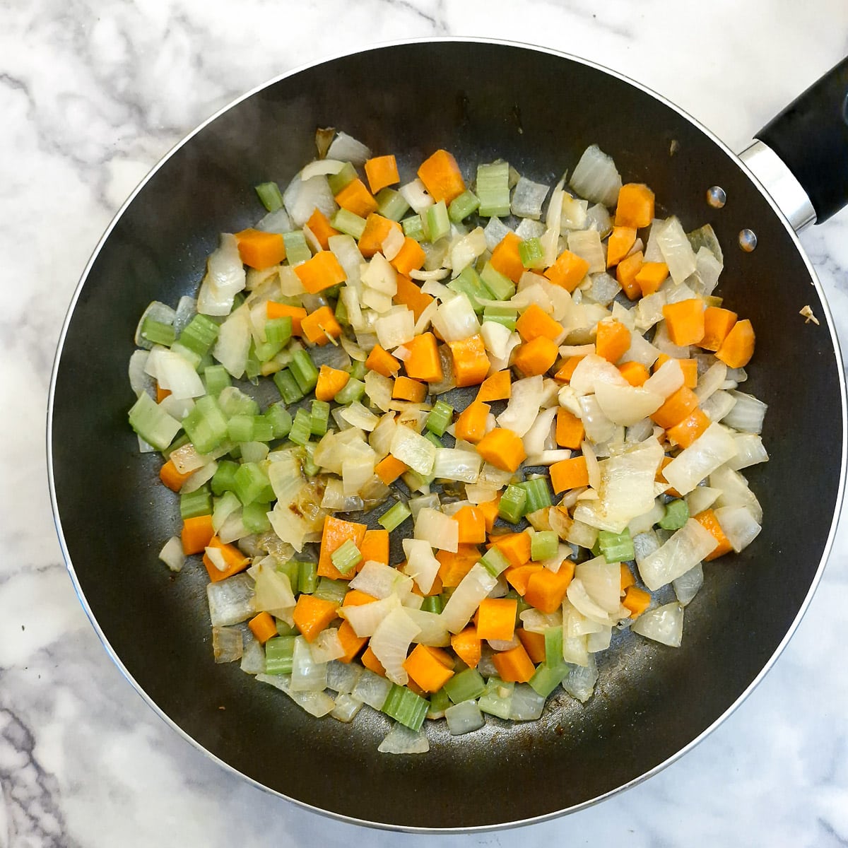Carrots and celery softening with onions in a frying pan.