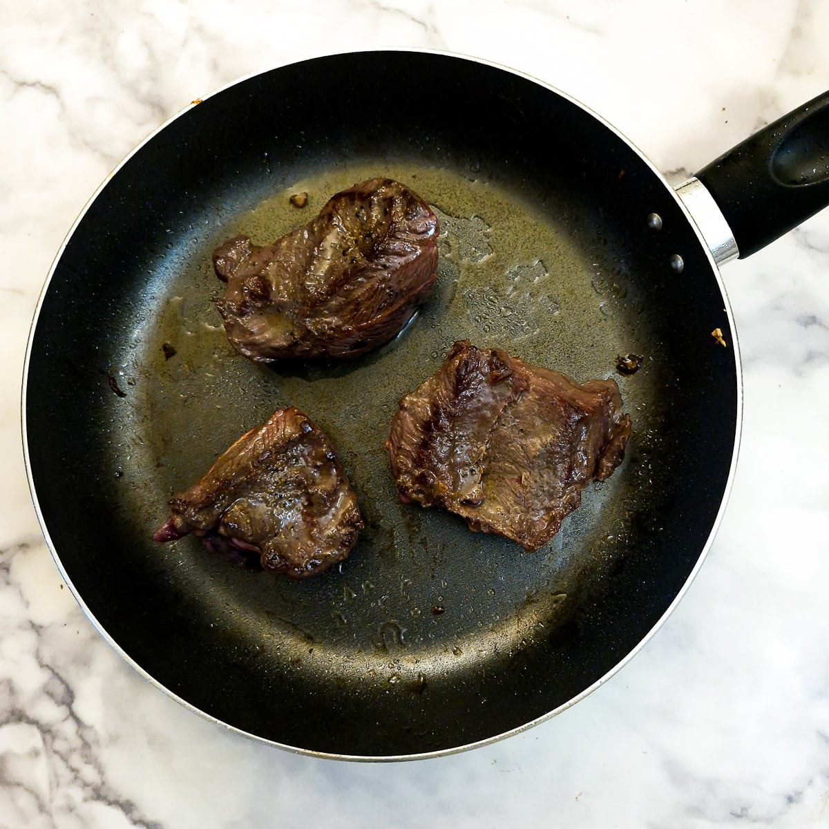 Beef cheeks browning in a frying pan.
