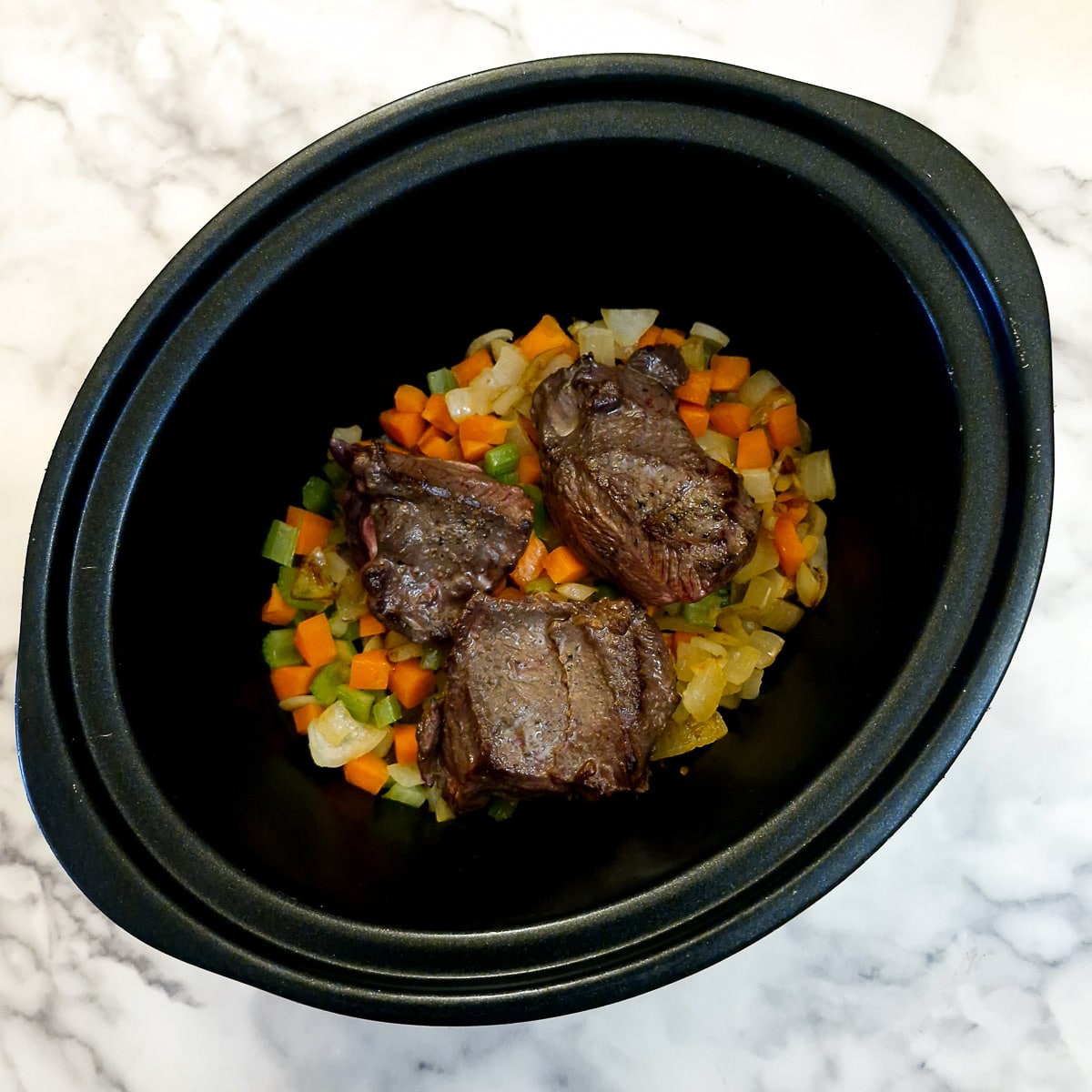 Beef cheeks added to vegetables in a slow cooker.