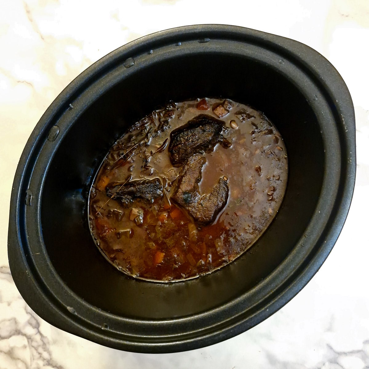 Cooked beef cheeks in a slow cooker.