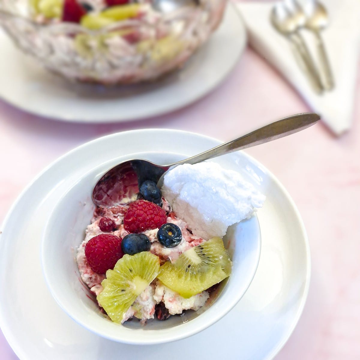 A helping of Eton mess topped with piees of fresh fruit in a small white bowl.