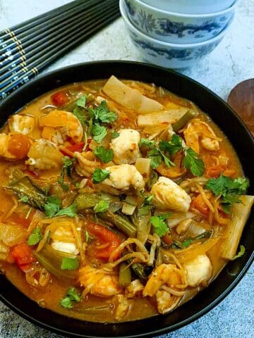 A black serving dish of Thai prawn and monkfish curry.