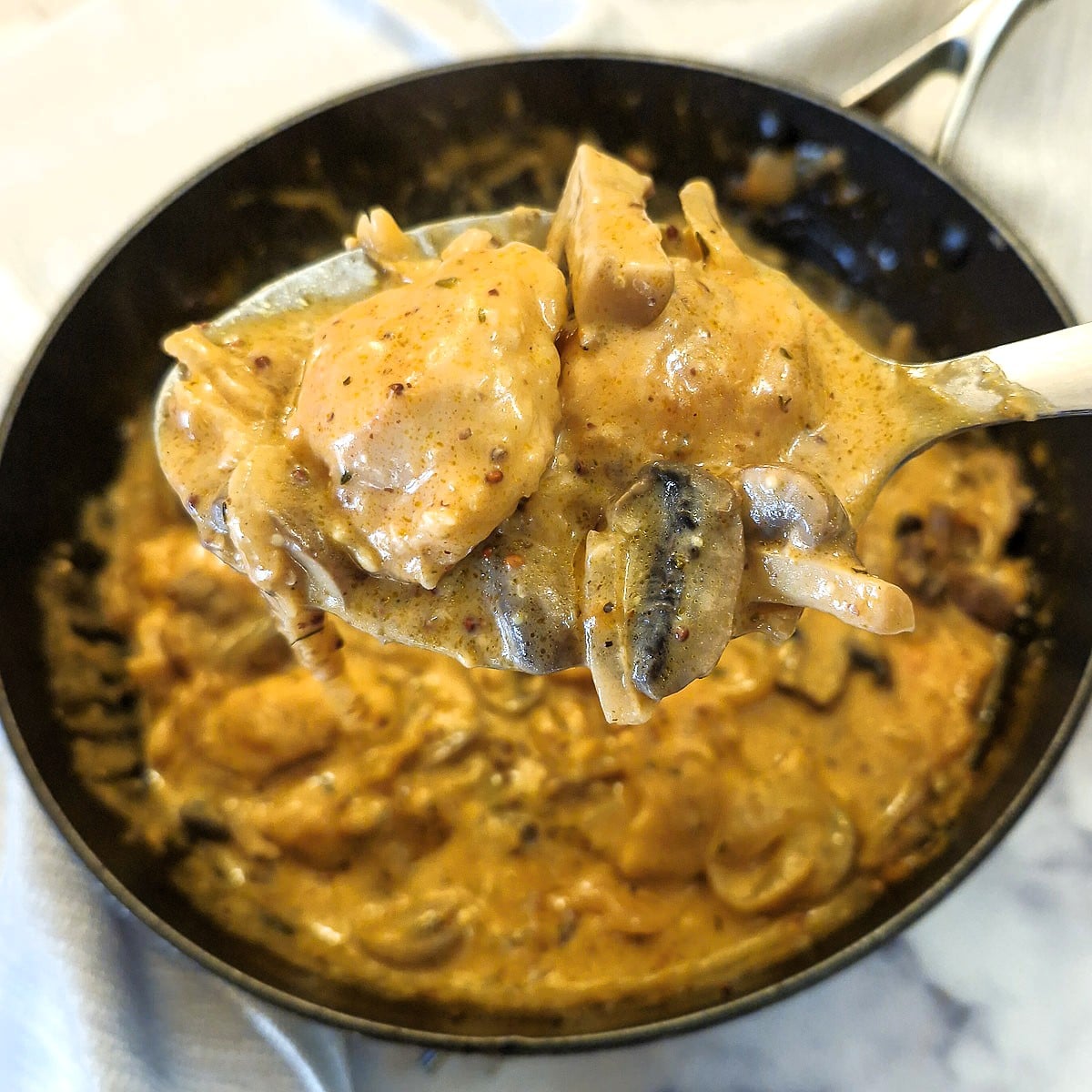 A spoonful of mushroom chicken being lifted from a pan.