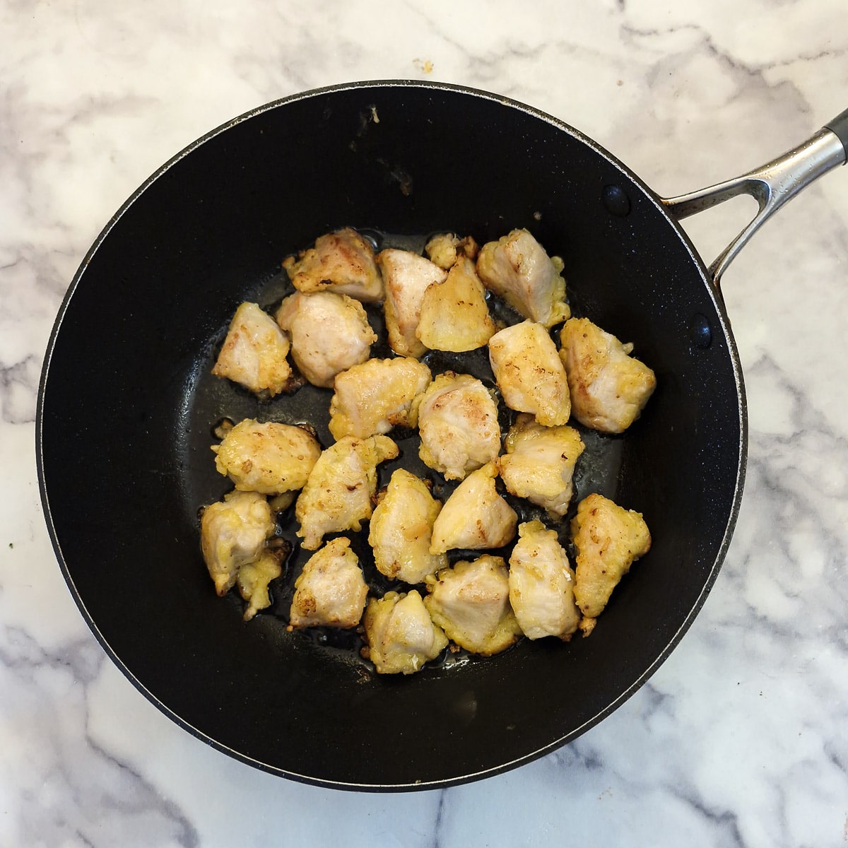 Lightly battered chicken pieces browning in a frying pan.