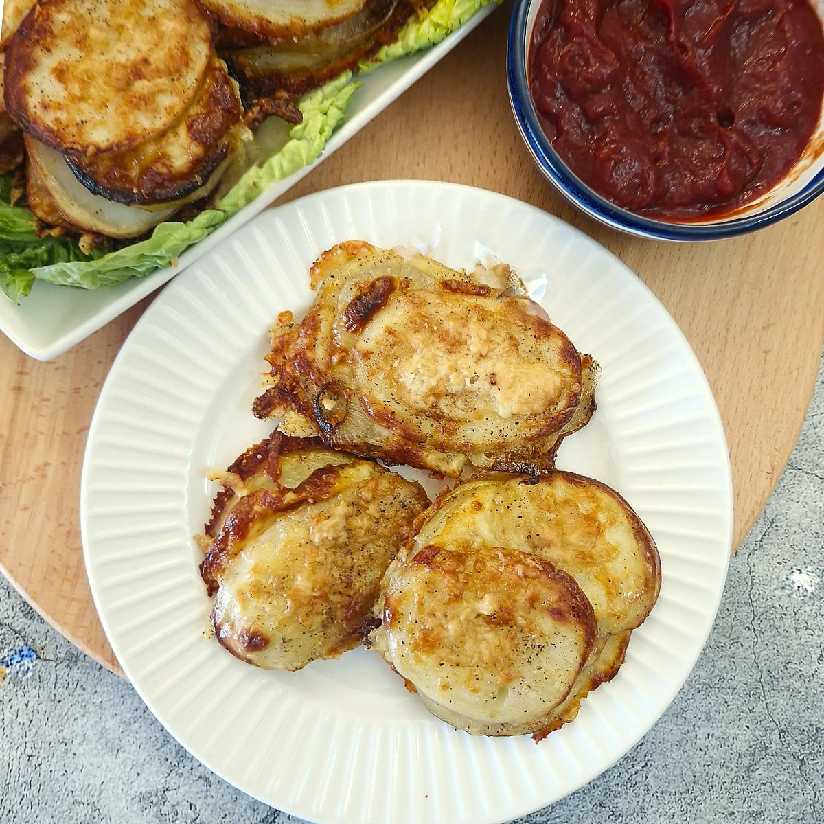 Three potato and onion slices on a white plate next to a bowl of tomato ketchup.