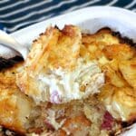 A spoonful of cheesy bacon and onion potato bake being lifted from a serving dish.