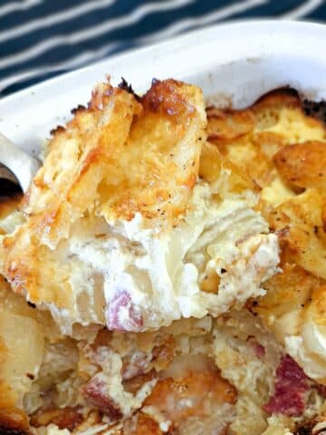 A spoonful of cheesy bacon and onion potato bake being lifted from a serving dish.