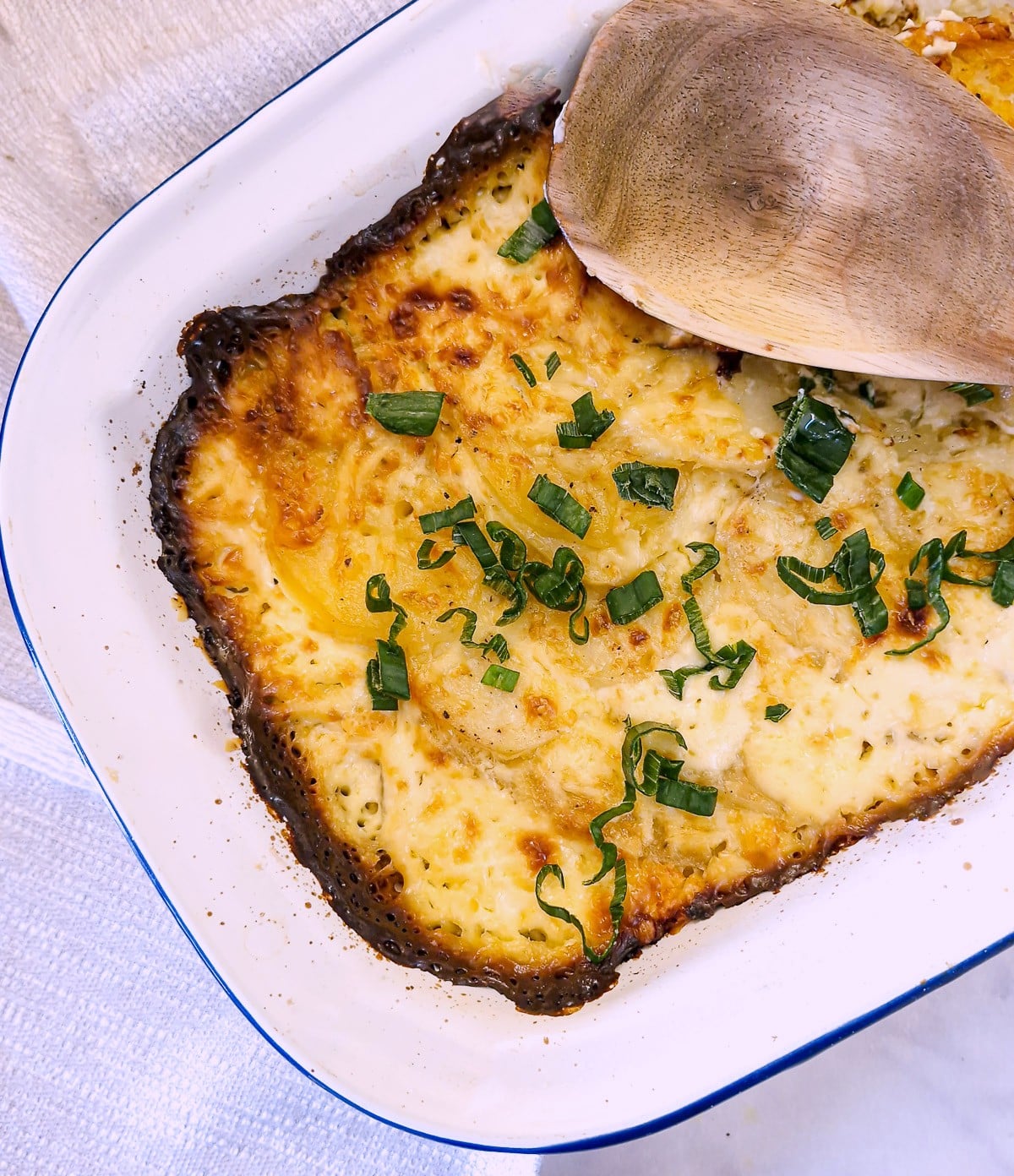 Overhead view of a cheese bacon and onion potato bake.  There is a large wooden spoon resting on top.