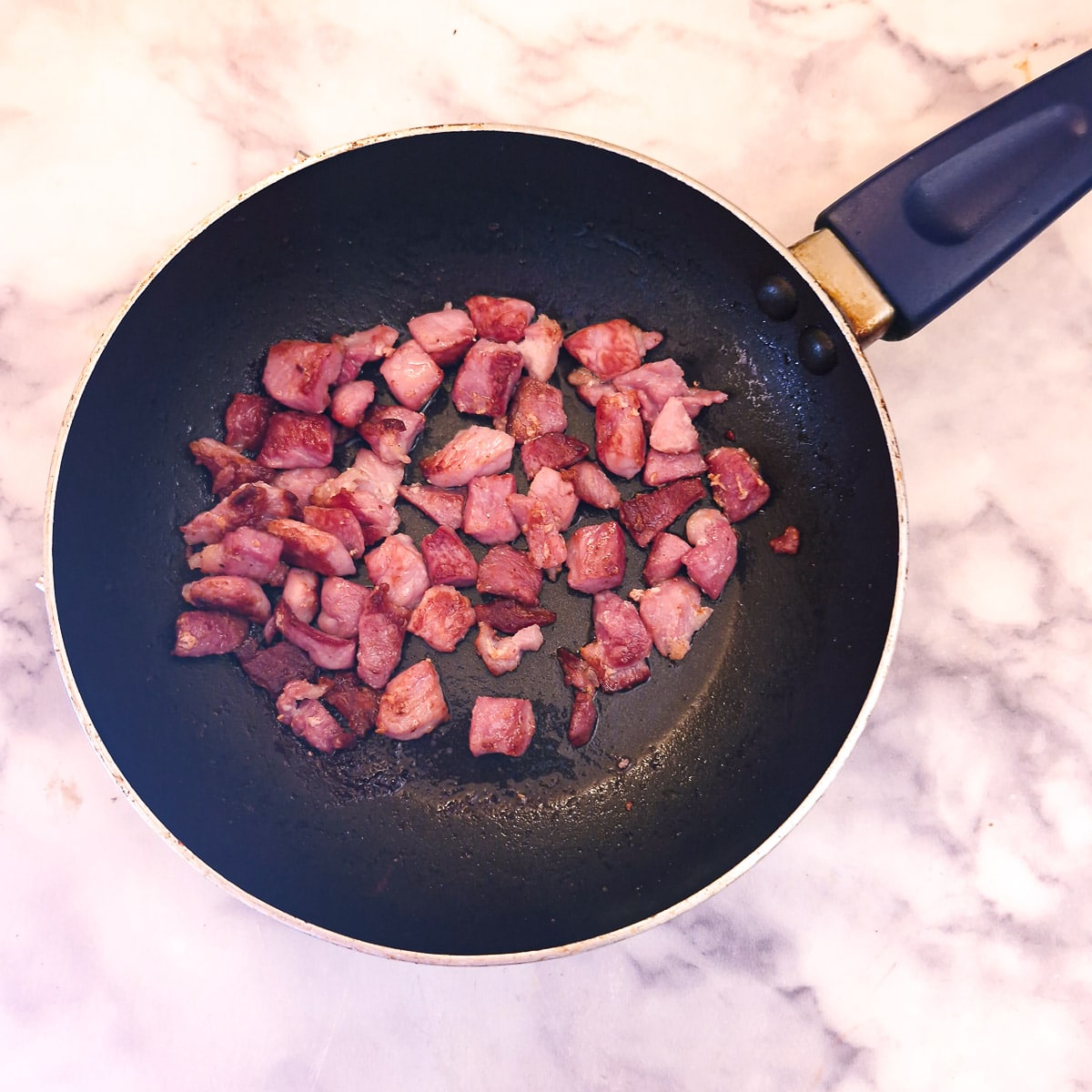 Pieces of bacon browning in a frying pan.