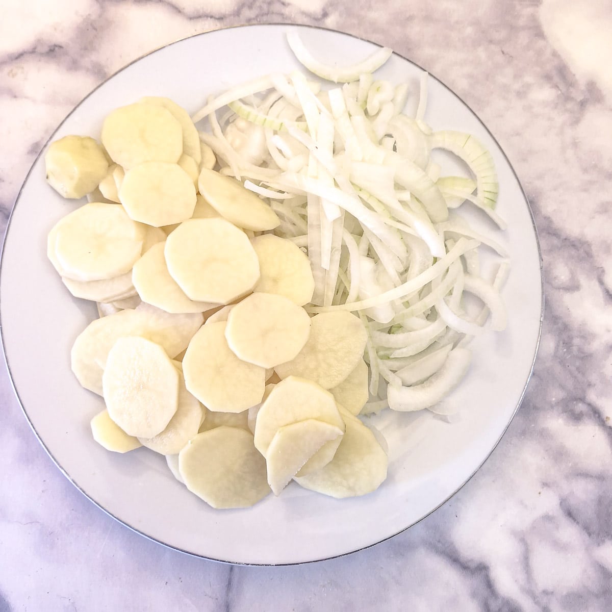 Thinly sliced potatoes and onions of a white plate.