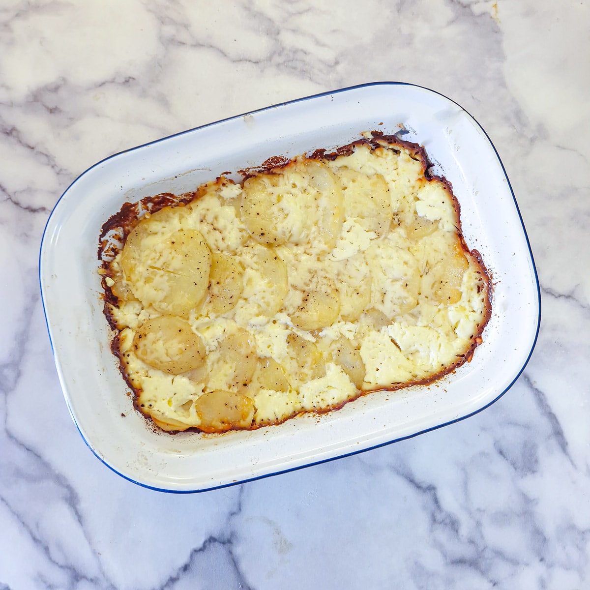 A part-baked potato bake in a white dish before the cheese topping  has been browned.