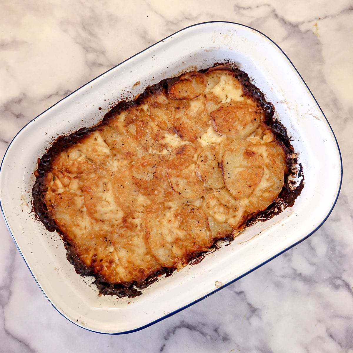 A nicely browned potato bake in a white enamel dish.