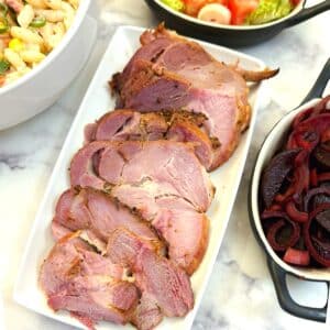 Slices of gammon on a white serving platter surrounded by dishes of salads.