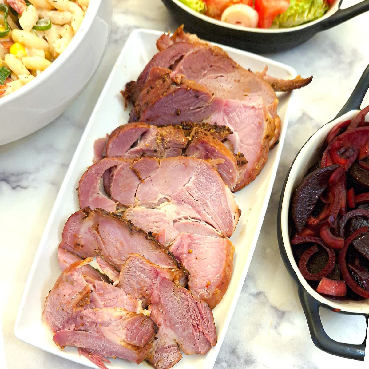 Slices of gammon on a white serving platter surrounded by dishes of salads.