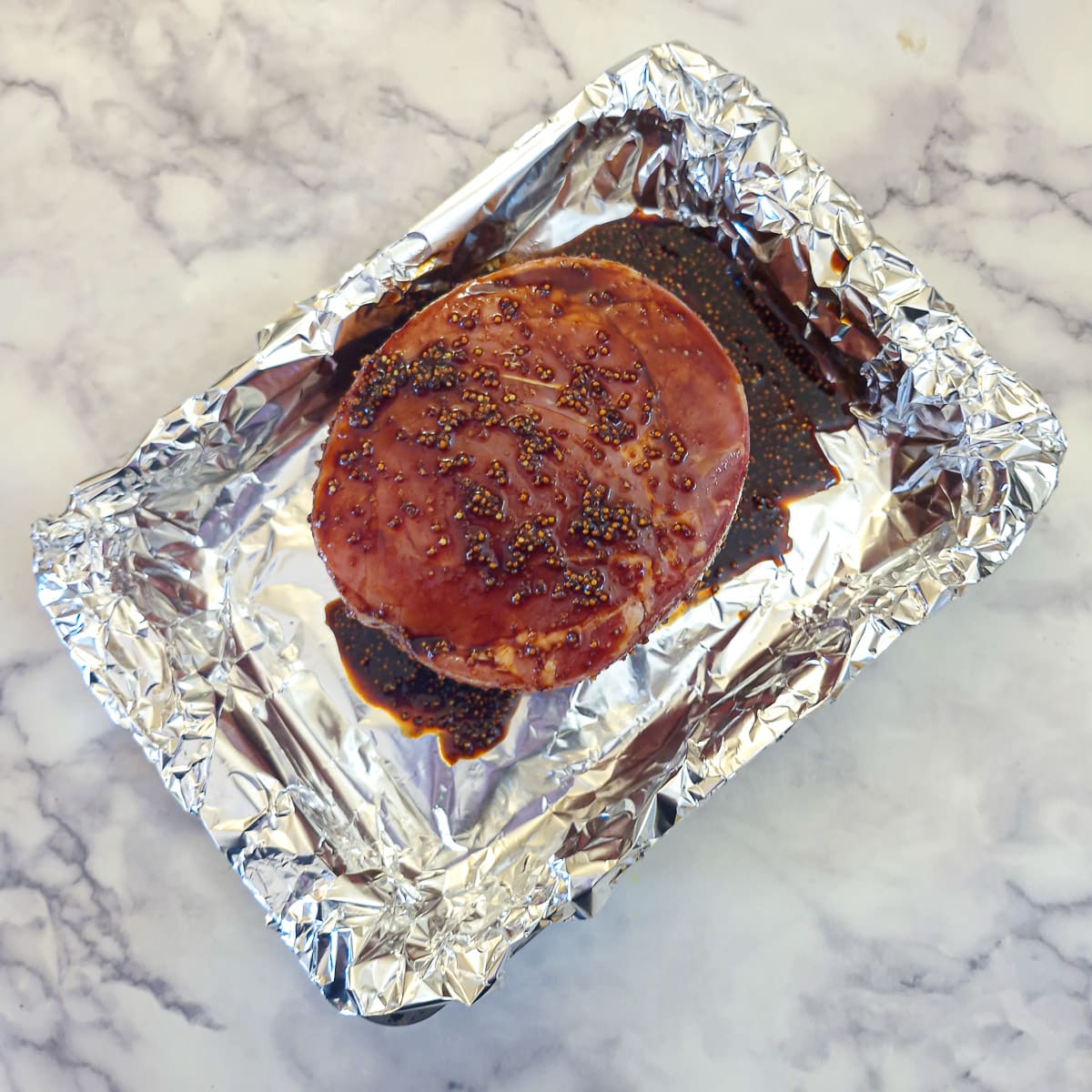 A joint of gammon covered with glaze in a foil-lined roasting dish.