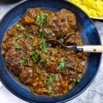 A blue serving dish with beef osso buco garnished with parsley.