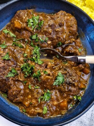A blue serving dish with beef osso buco garnished with parsley.