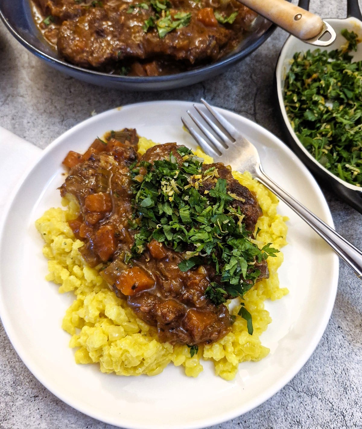 Beef shin osso buco on a pile of saffron risotto and garnished with gremolata.