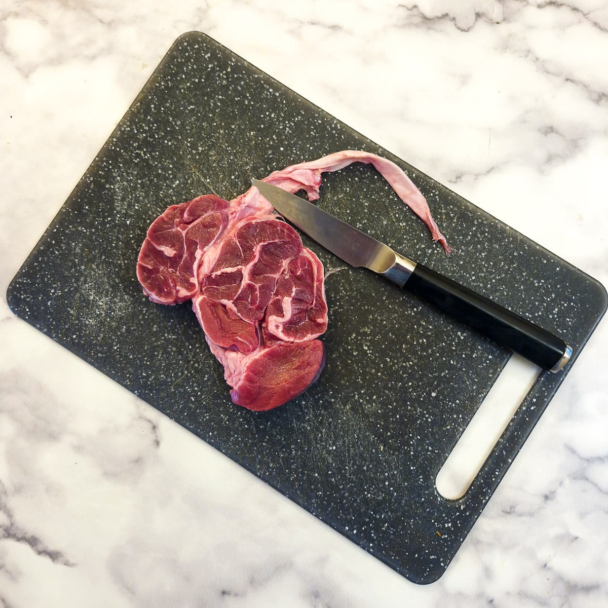 Thick silver skin being removed from a piece of beef shin with a sharp knife.