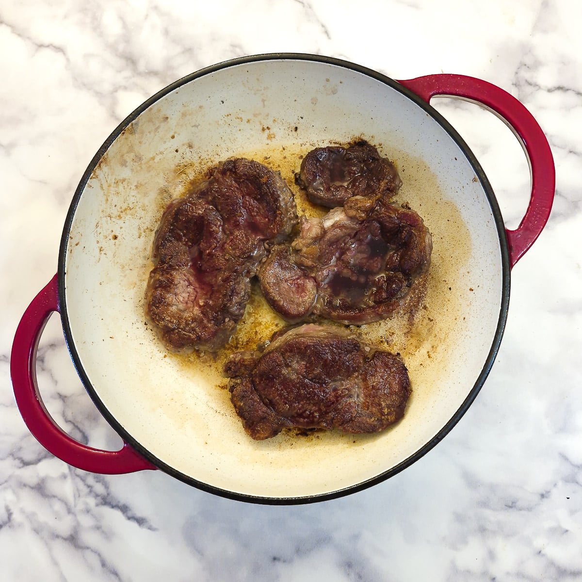 Beef shin being browned in a large casserole dish.