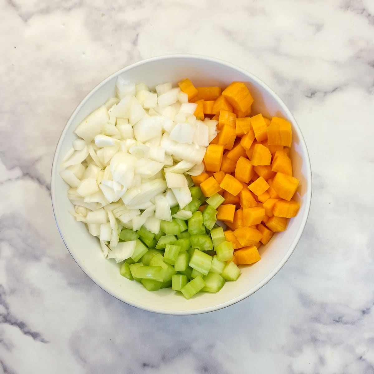 A white bowl containing finely chopped carrots, celery and onions.