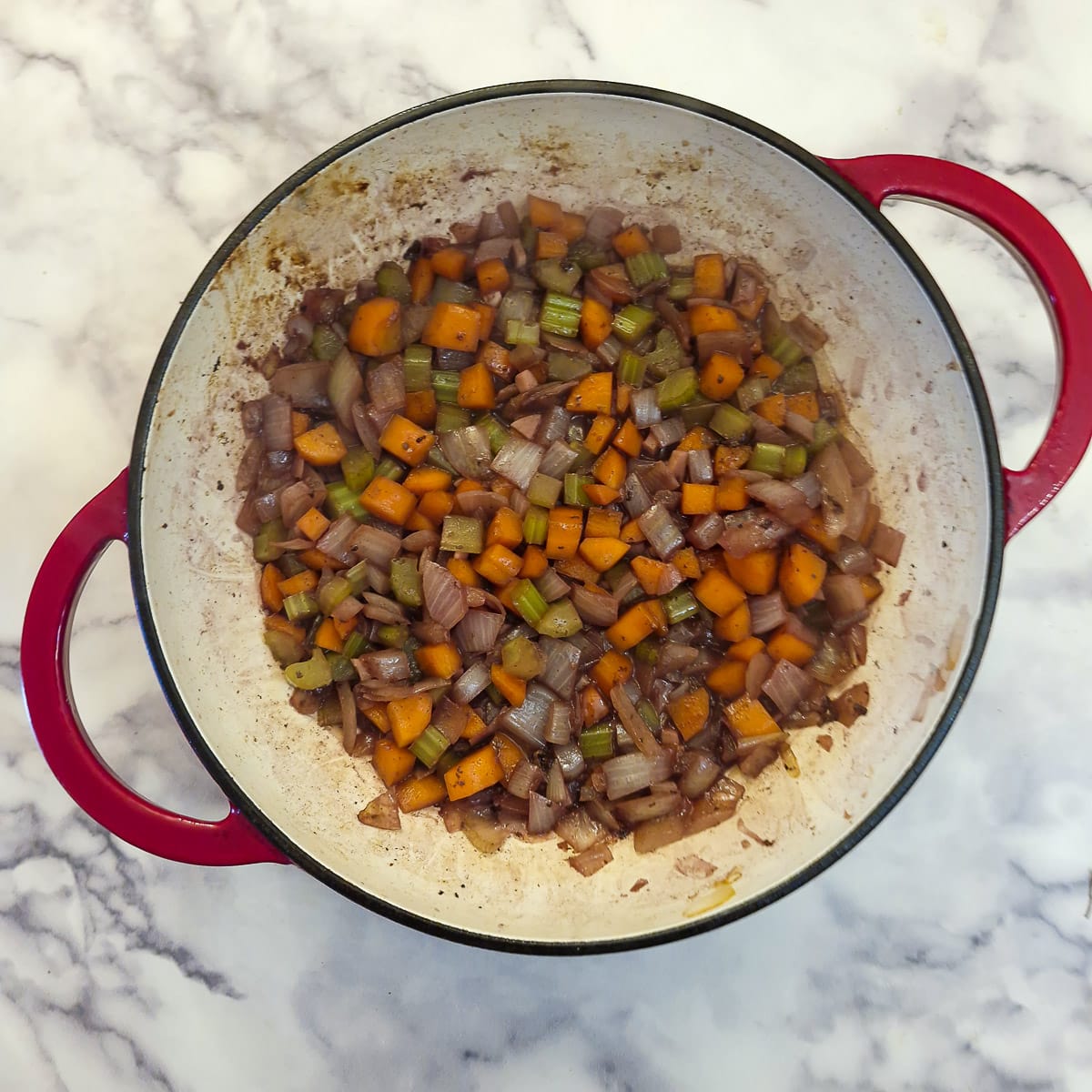 Red wine reducing with carrots, celery and onions in a casserole dish.