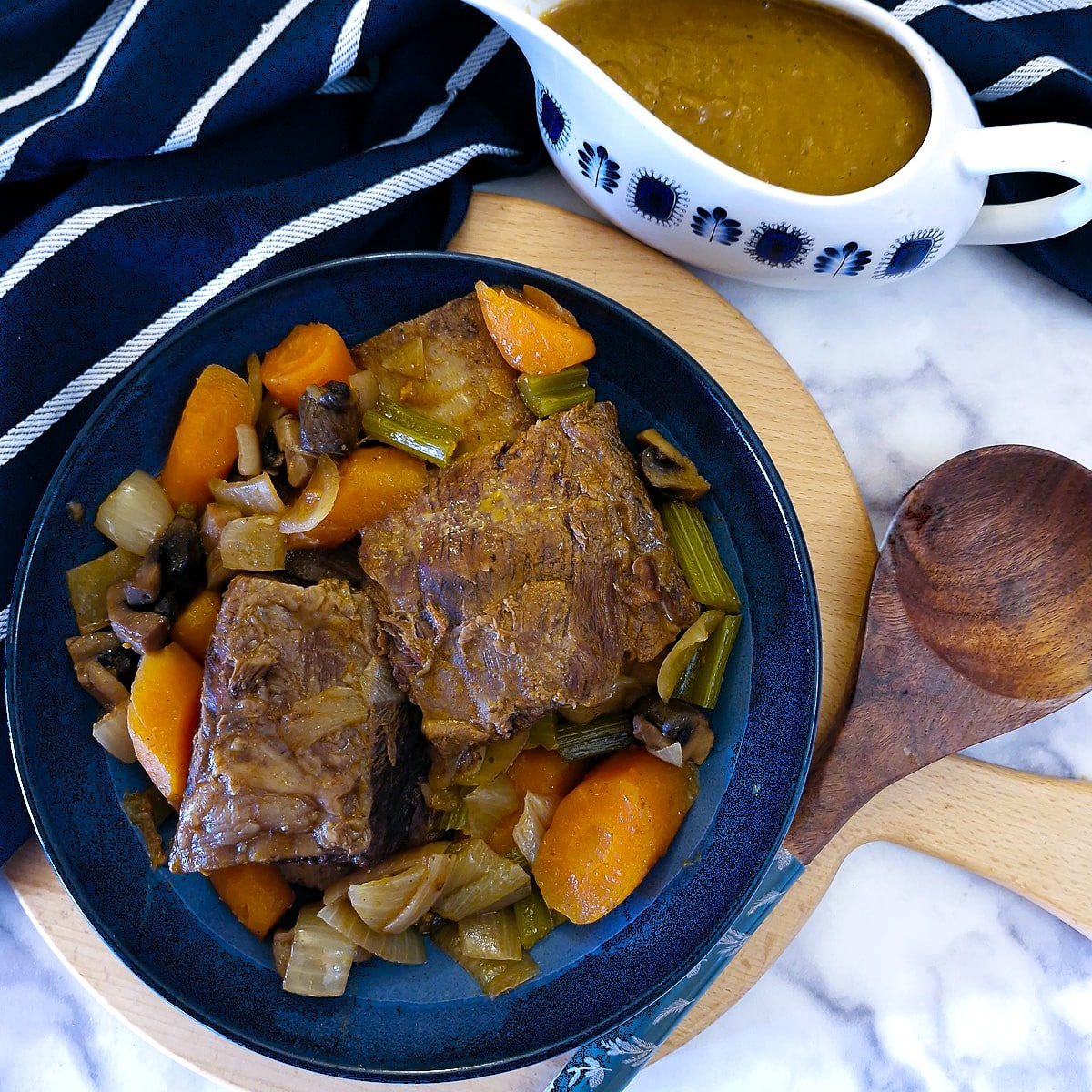 Overhead shot of 2 pieces of beef short rib in a blue serving dish.  There is a jug of gravy alongside.