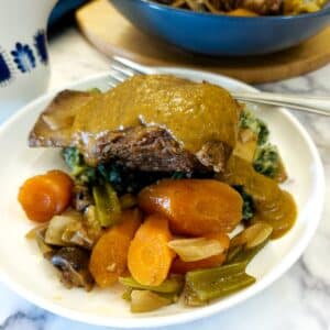 A dinner plate of beef short rib covered in rich vegetable gravy on a pile of spring green mash with vegetables.