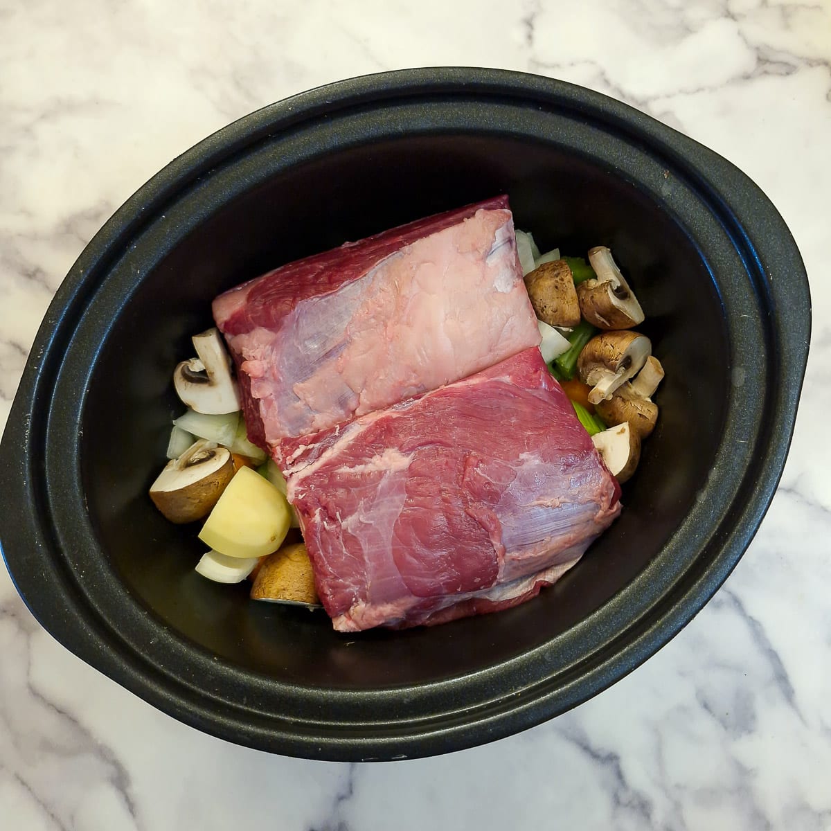 Two large beef short ribs on top of chopped vegetables in a slow cooker.