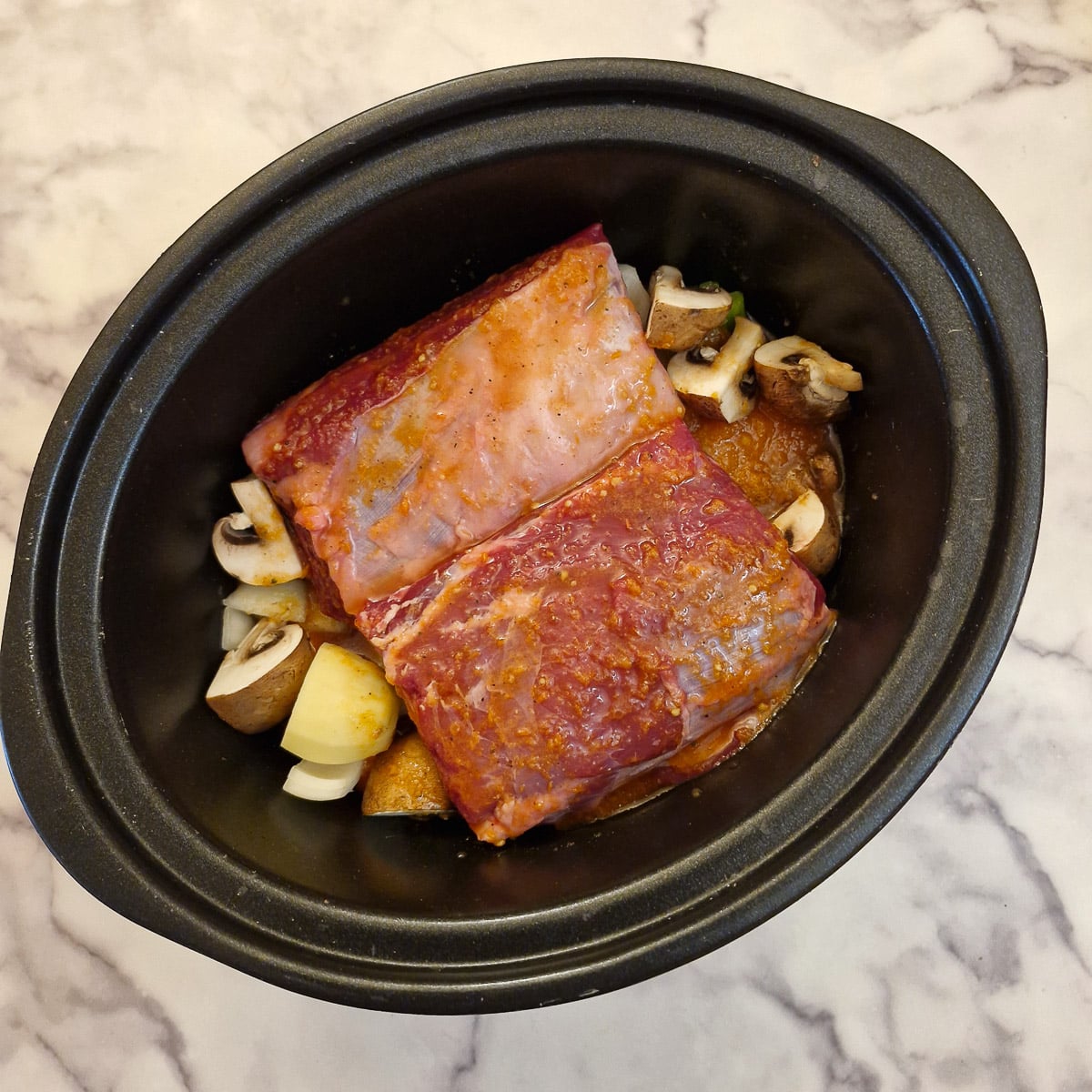 Stock covering the beef short ribs in a slow cooker.