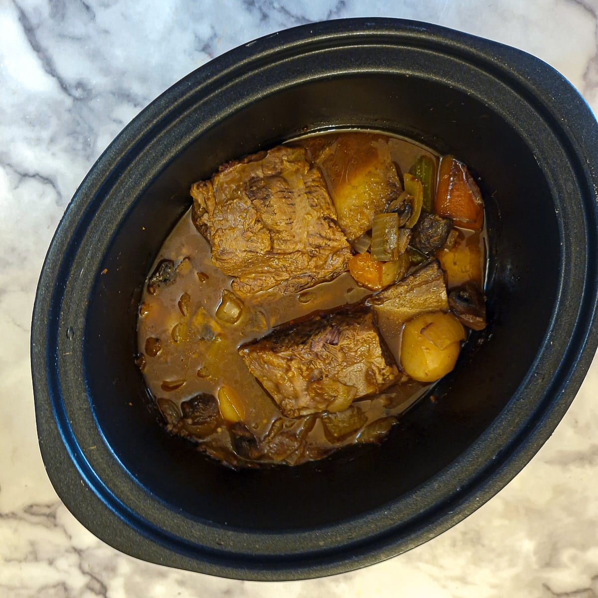 Fully cooked beef short ribs in a slow cooker.