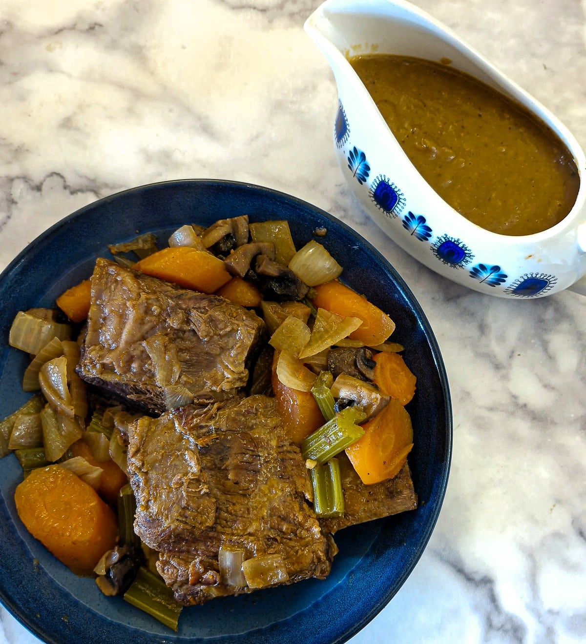 Beef short ribs on a serving plate alongside a jug of gravy,