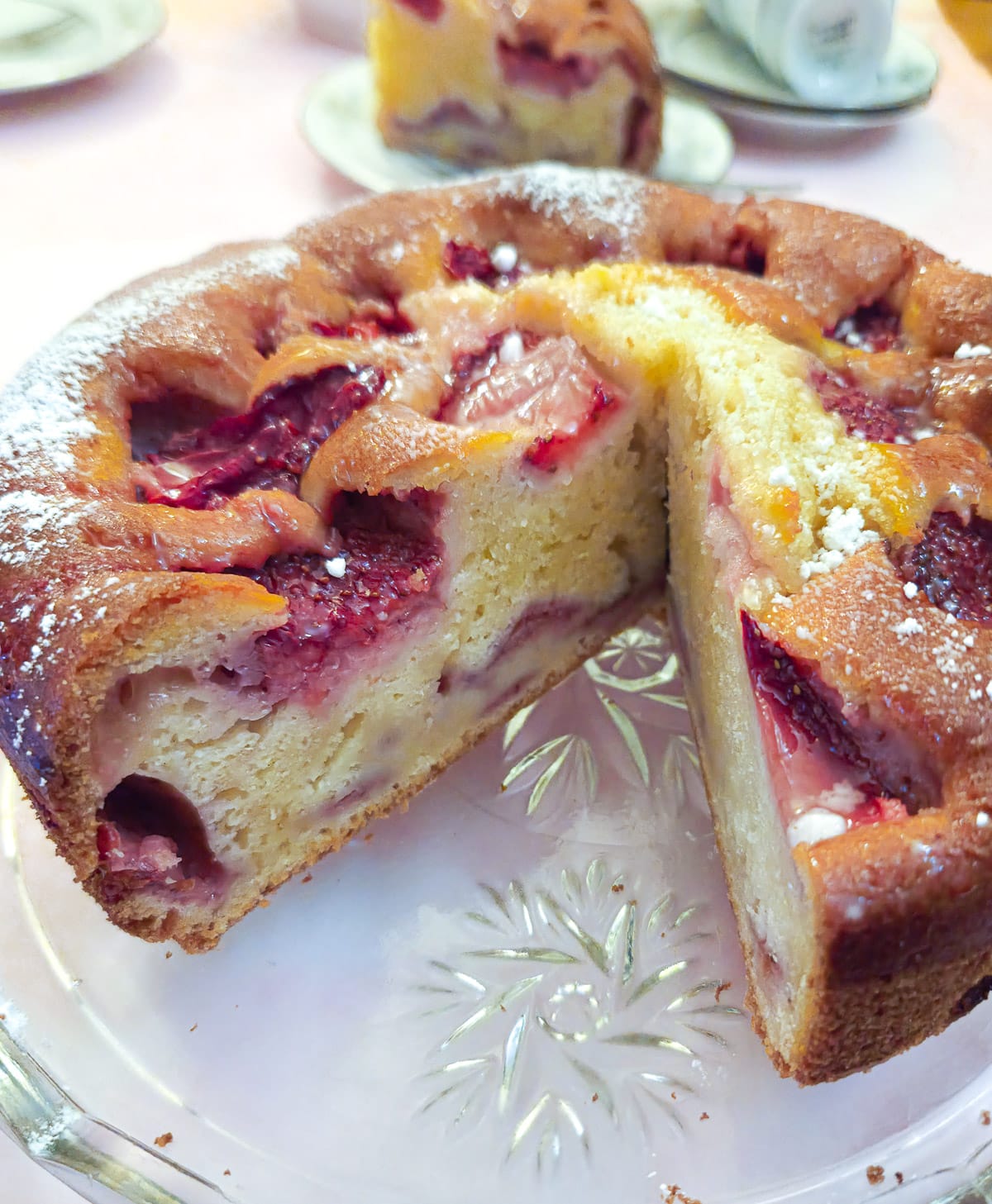 A strawberry mascarpone cake on a glass platter with a slice removed to show the inside of the cake.